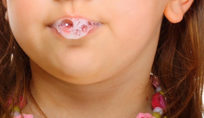 Nahaufnahme eines Kindes mit sch&auml;umendem Speichel an den Lippen. Das Kind hat braune Haare und tr&auml;gt eine bunte Halskette.